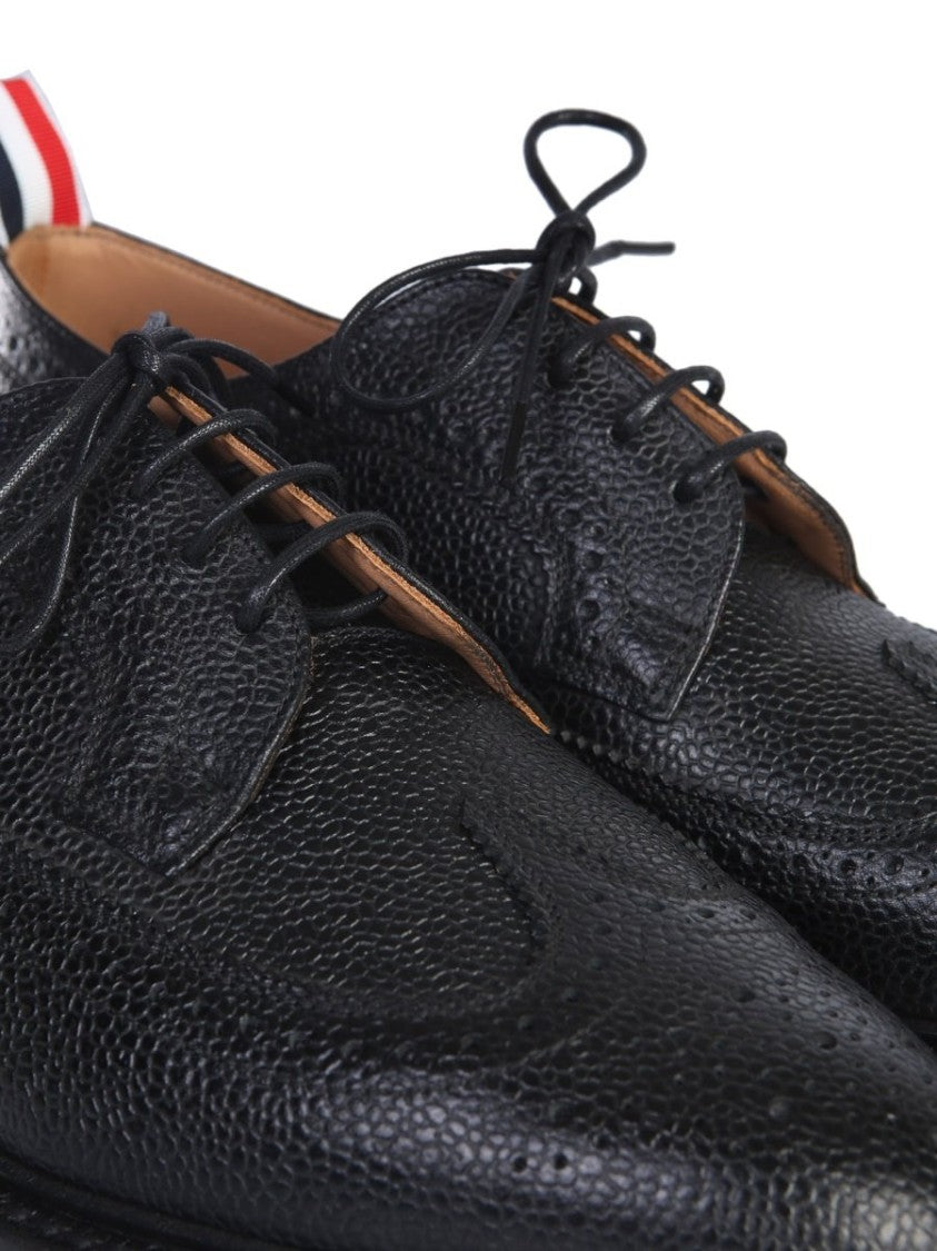 Thom Browne offers a classic dress shoe crafted from premium textured calf leather, featuring intricate brogue detailing along the toe and sides. This sophisticated design showcases a sleek silhouette, low heel, and practical lace-up closure, making it id