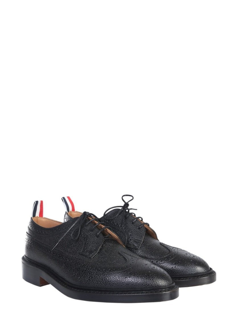 Thom Browne offers a classic dress shoe crafted from premium textured calf leather, featuring intricate brogue detailing along the toe and sides. This sophisticated design showcases a sleek silhouette, low heel, and practical lace-up closure, making it id