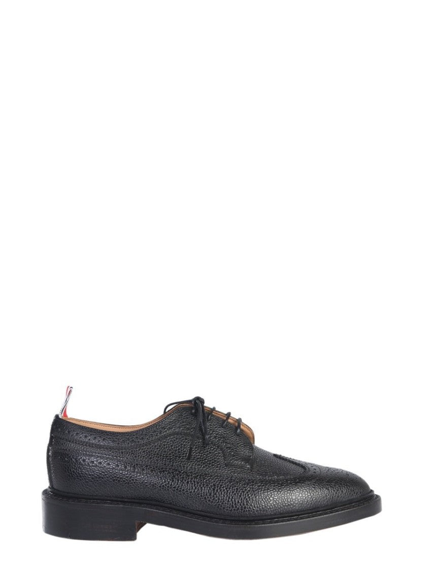 Thom Browne offers a classic dress shoe crafted from premium textured calf leather, featuring intricate brogue detailing along the toe and sides. This sophisticated design showcases a sleek silhouette, low heel, and practical lace-up closure, making it id