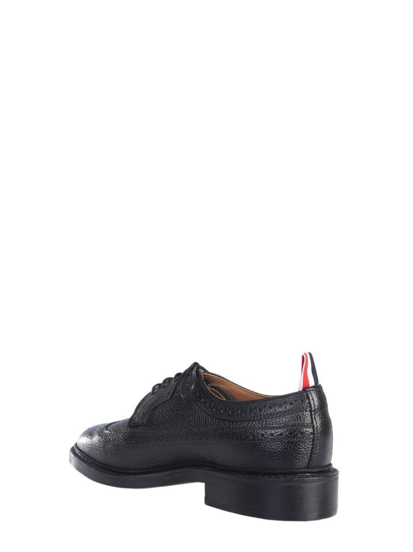 Thom Browne offers a classic dress shoe crafted from premium textured calf leather, featuring intricate brogue detailing along the toe and sides. This sophisticated design showcases a sleek silhouette, low heel, and practical lace-up closure, making it id
